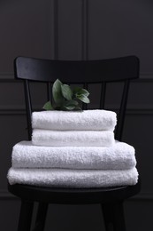 Photo of Stacked soft towels and green leaves on black chair indoors