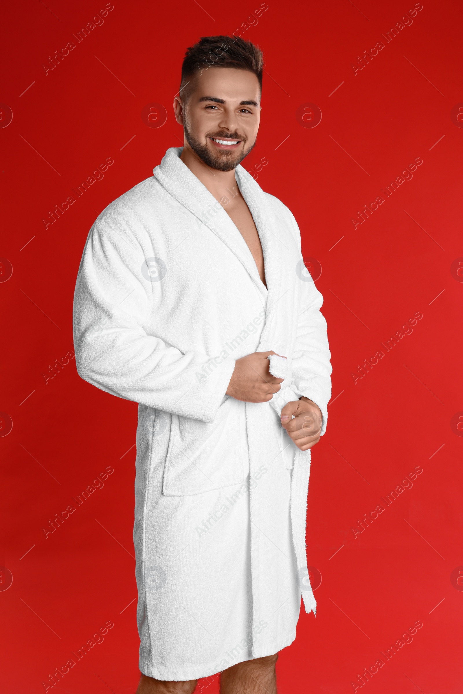 Photo of Happy young man in bathrobe on red background