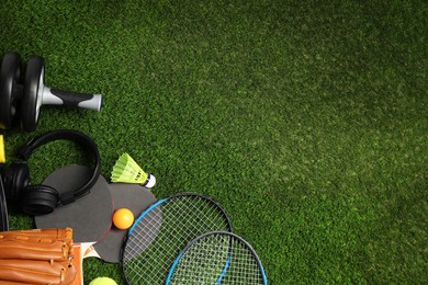 Different sports equipment on green grass, flat lay. Space for text