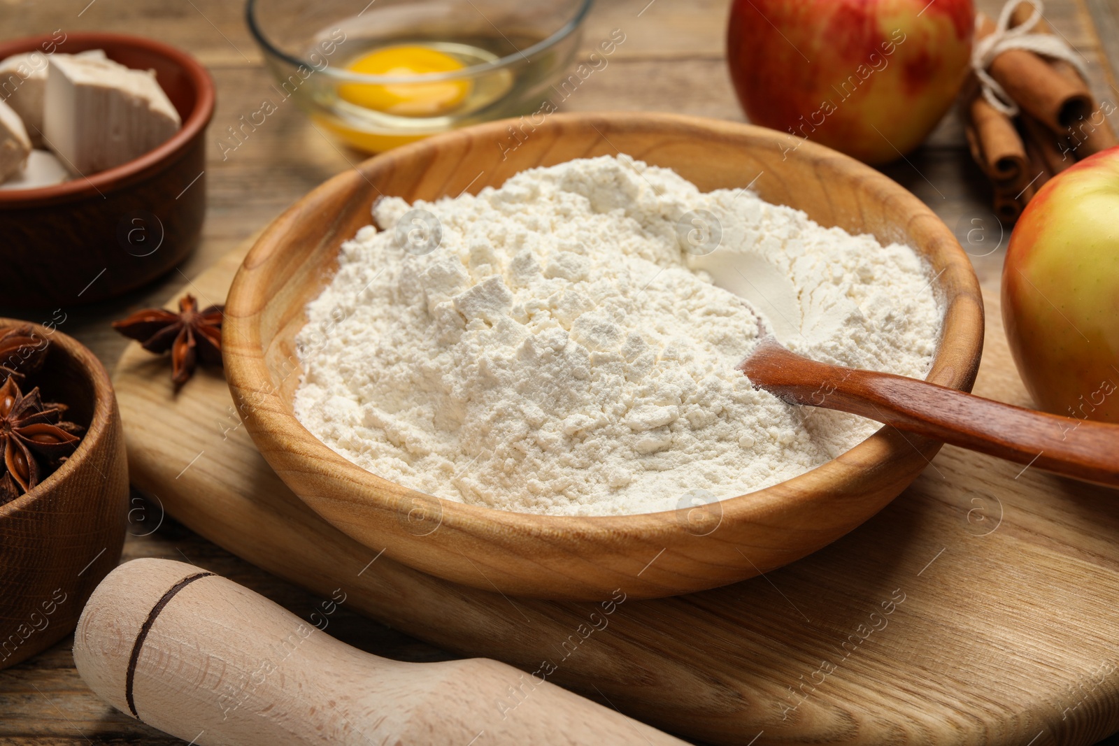 Photo of Bowl with flour, rolling pin and ingredients on wooden table, closeup. Cooking yeast cake