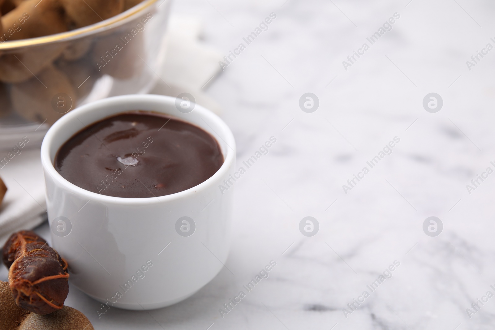 Bowl of tamarind sauce and fresh pods on white marble table. Space for text Photo of Bowl of tamarind sauce and fresh pods on white marble table. Space for text