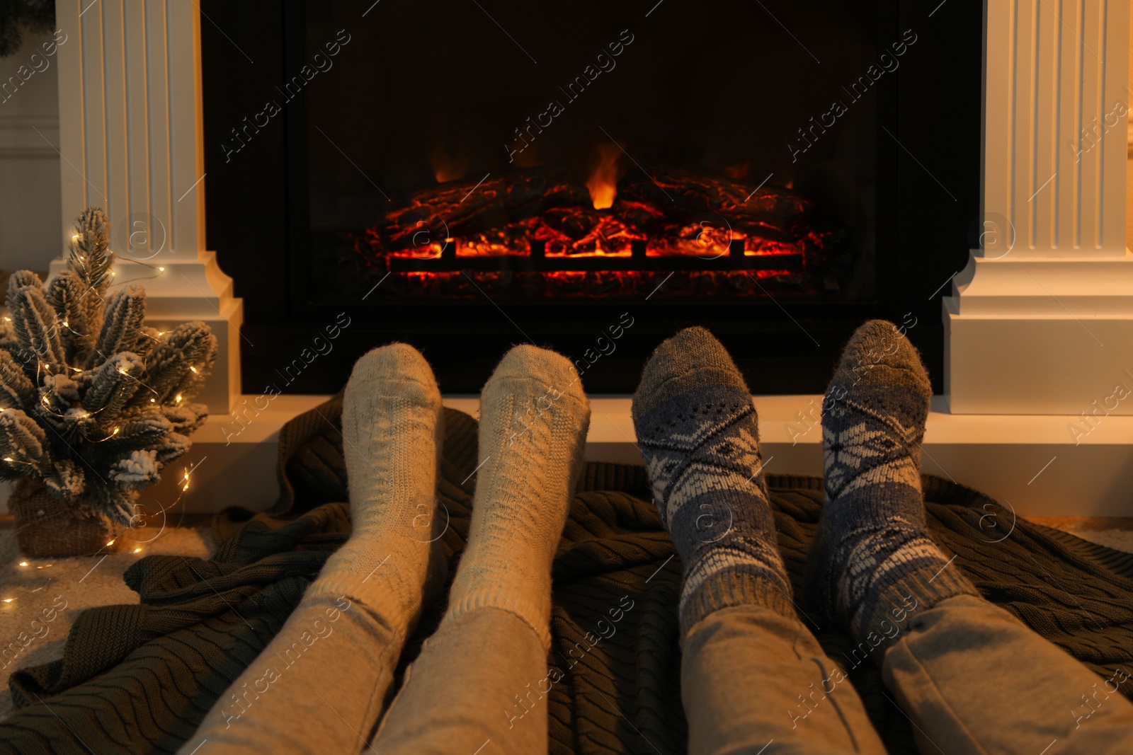 Photo of Couple in warm socks resting near fireplace at home, closeup