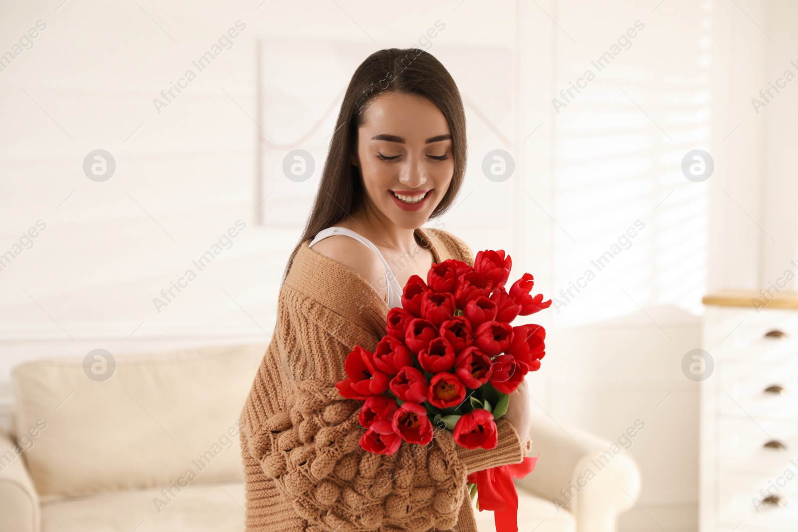 Photo of Happy woman with red tulip bouquet at home. 8th of March celebration