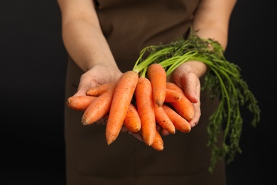 Photo of Young woman holding ripe carrots on black background, closeup