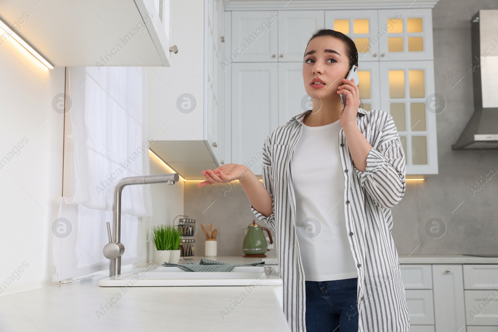 Photo of Woman talking on phone near sink in kitchen