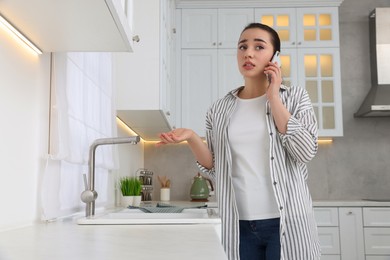 Photo of Woman talking on phone near sink in kitchen