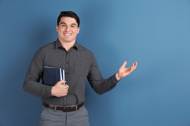 Portrait of male teacher with notebooks on color background