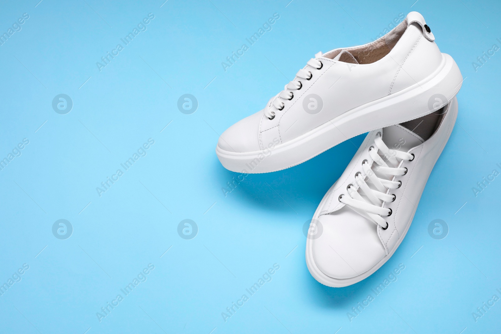 Photo of Pair of stylish white sneakers on light blue background, top view. Space for text