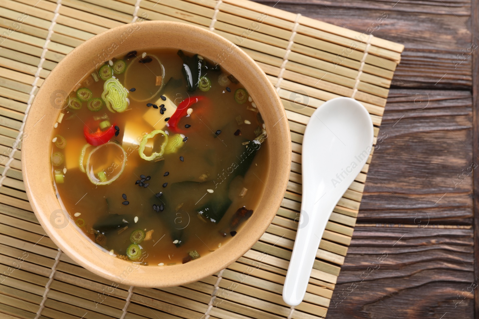 Photo of Bowl of delicious miso soup with tofu and spoon on wooden table, top view