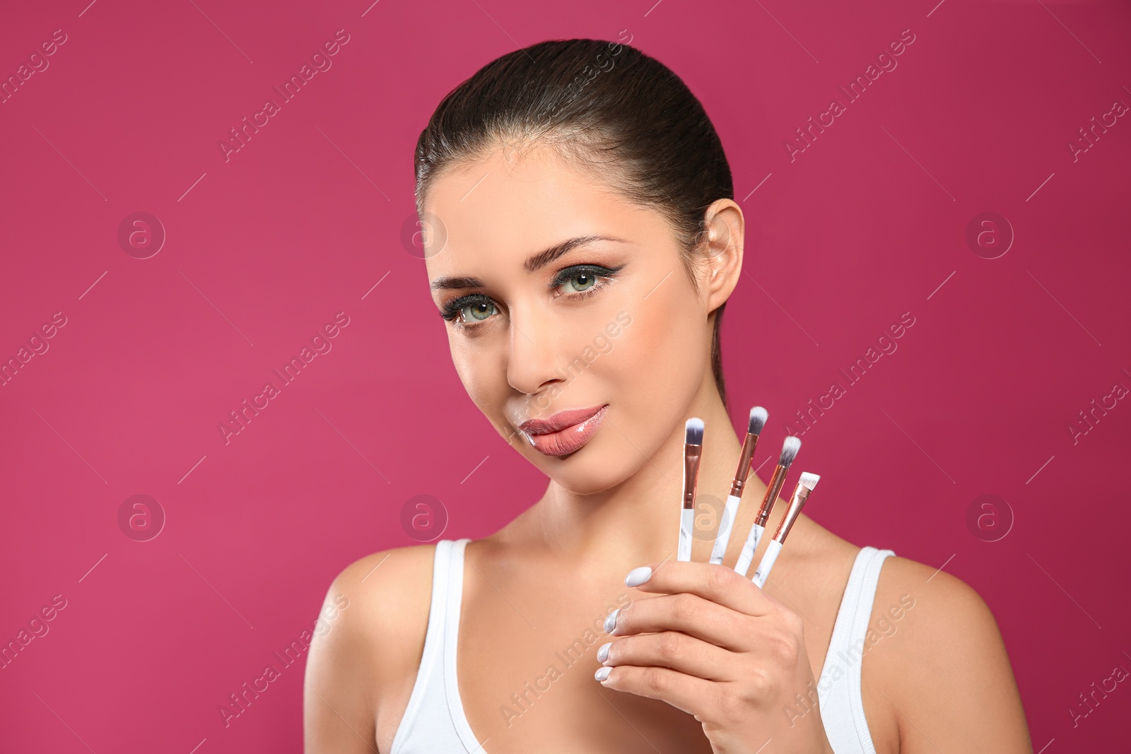 Photo of Beautiful woman with makeup brushes on pink background