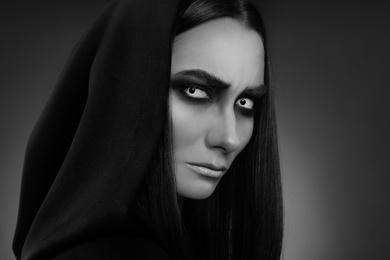 Photo of Mysterious witch with spooky eyes on dark background, closeup. Black and white effect