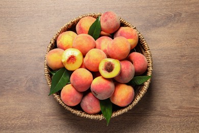 Photo of Cut and whole fresh ripe peaches with green leaves in basket on wooden table, top view