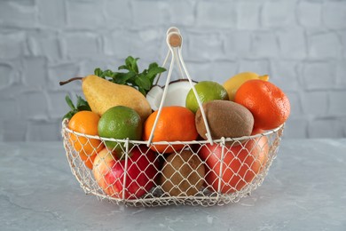 Metal basket with different ripe fruits on grey table