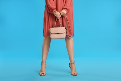 Photo of Young woman with stylish pink bag on light blue background, closeup
