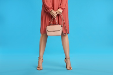 Young woman with stylish pink bag on light blue background, closeup