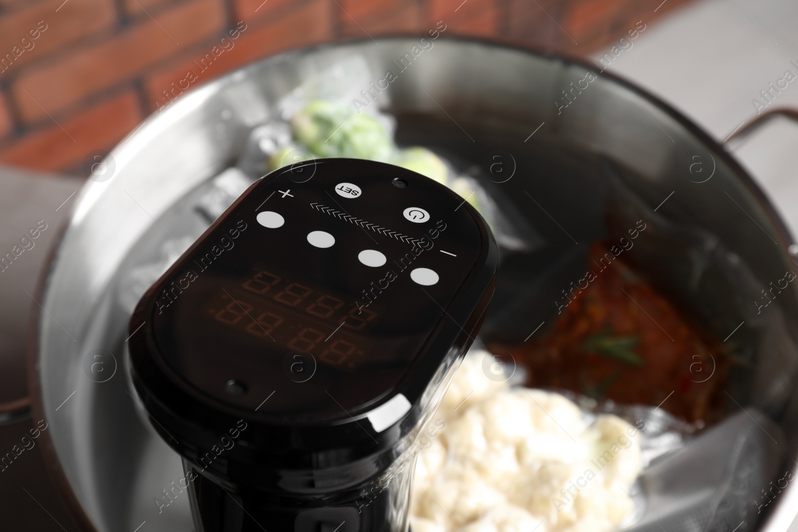Photo of Thermal immersion circulator and vacuum packed ingredients in pot on table, closeup. Sous vide cooking
