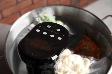Photo of Thermal immersion circulator and vacuum packed ingredients in pot on table, closeup. Sous vide cooking