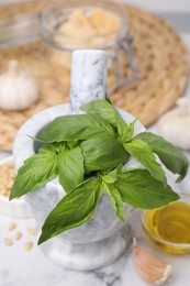 Photo of Fresh basil in mortar on white marble table, closeup. Ingredients for pesto sauce