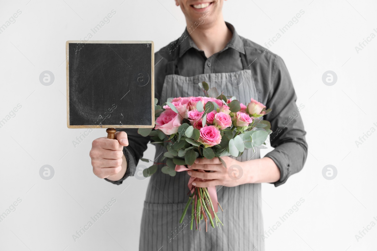 Photo of Male florist holding small chalkboard and bouquet on light background