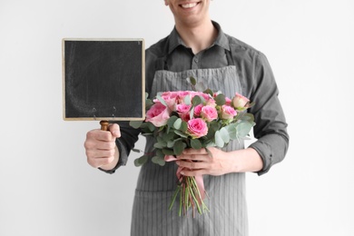 Photo of Male florist holding small chalkboard and bouquet on light background