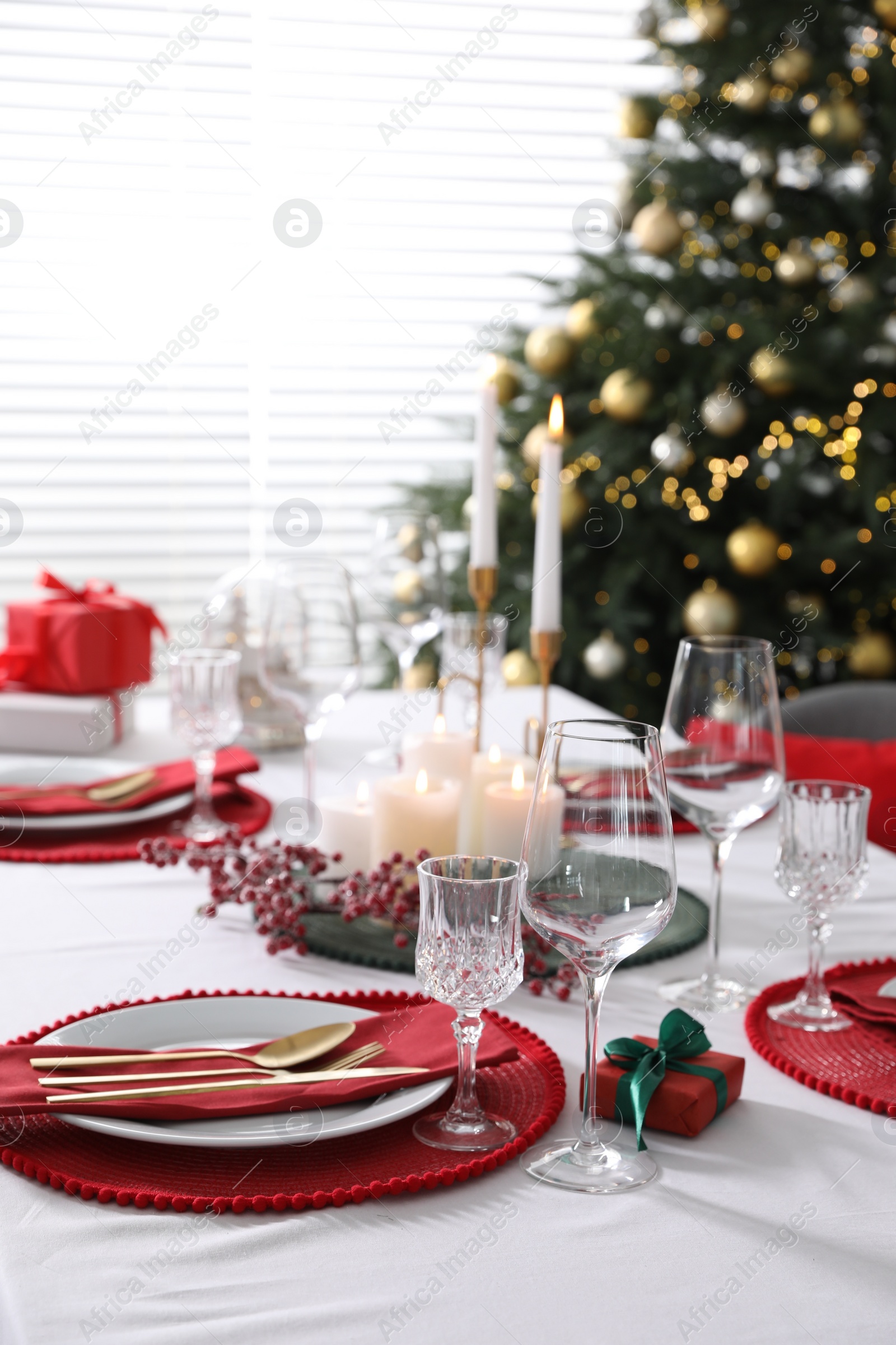 Photo of Christmas table setting with burning candles, gift box and dishware indoors