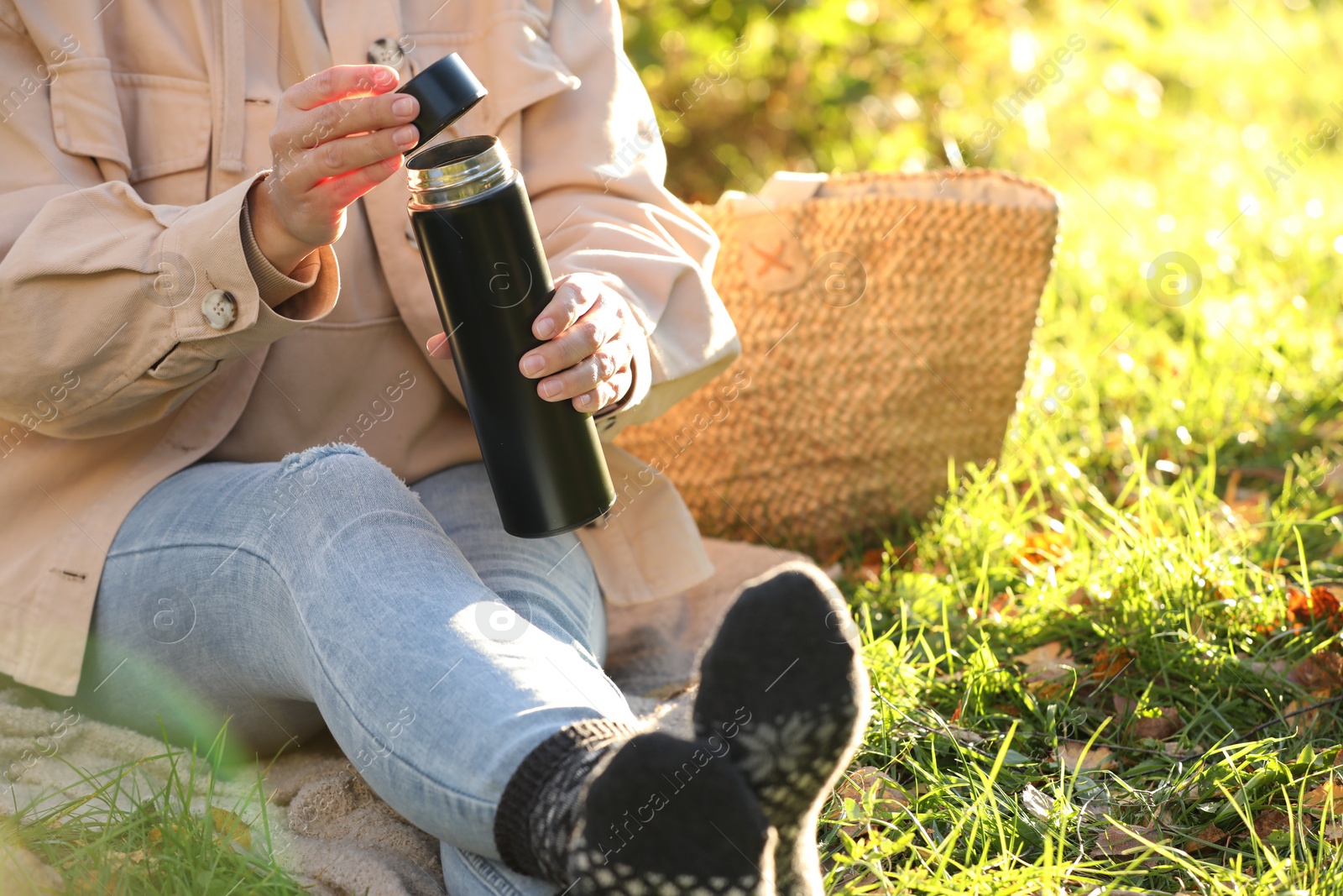 Photo of Picnic time. Woman opening thermos on green grass outdoors, closeup