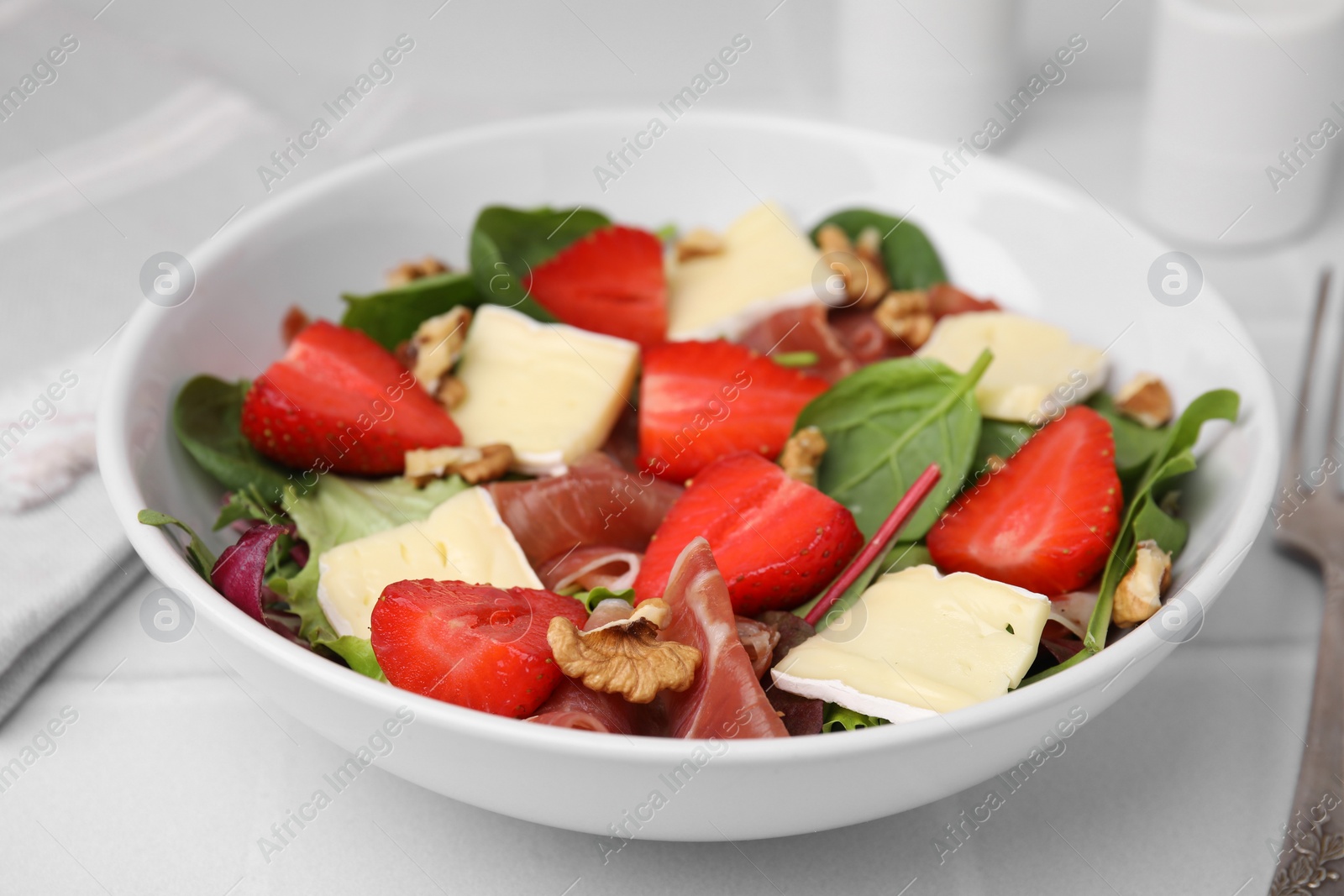 Photo of Tasty salad with brie cheese, prosciutto, strawberries and walnuts on white table, closeup