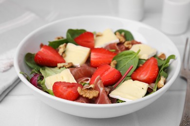 Tasty salad with brie cheese, prosciutto, strawberries and walnuts on white table, closeup