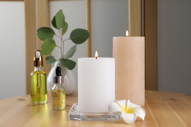 Photo of Burning candles, essential oil and plumeria flower on wooden table