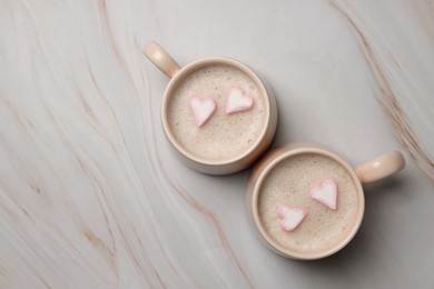 Cups of aromatic coffee with heart shaped marshmallows on white marble table, flat lay. Space for text