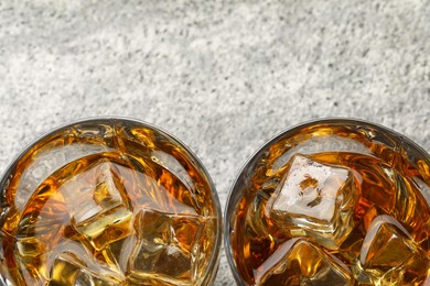 Photo of Whiskey and ice cubes in glasses on grey textured table, top view. Space for text