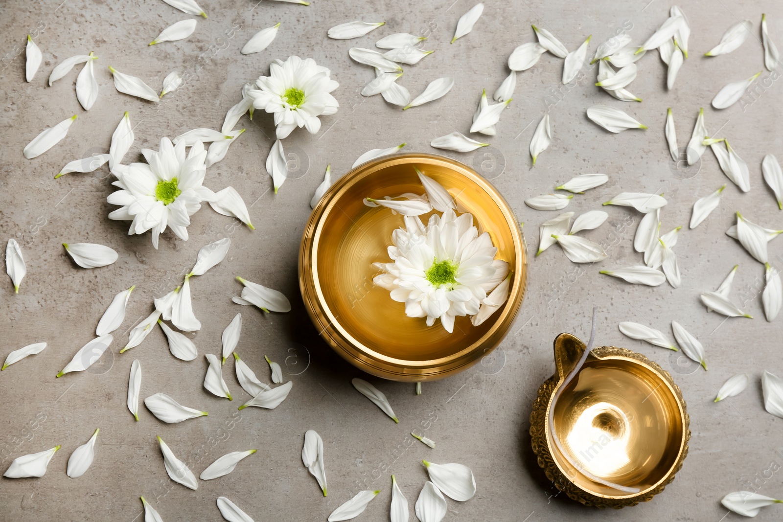 Photo of Flat lay composition with golden singing bowl and flowers on grey table. Sound healing