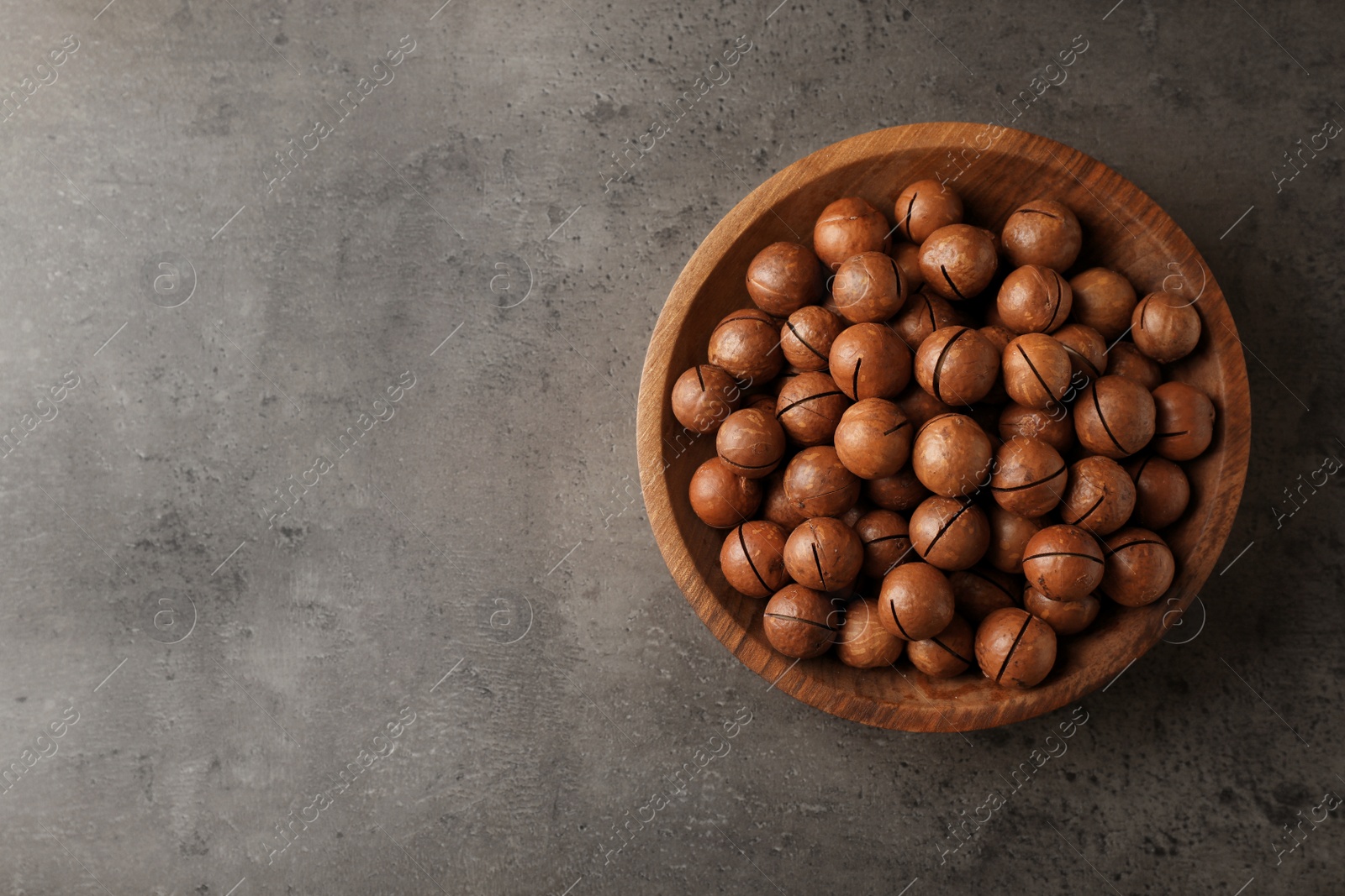 Photo of Plate with organic Macadamia nuts and space for text on grey background, top view