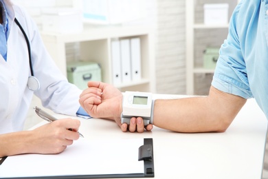 Photo of Doctor checking mature man's pulse with medical device in hospital, closeup