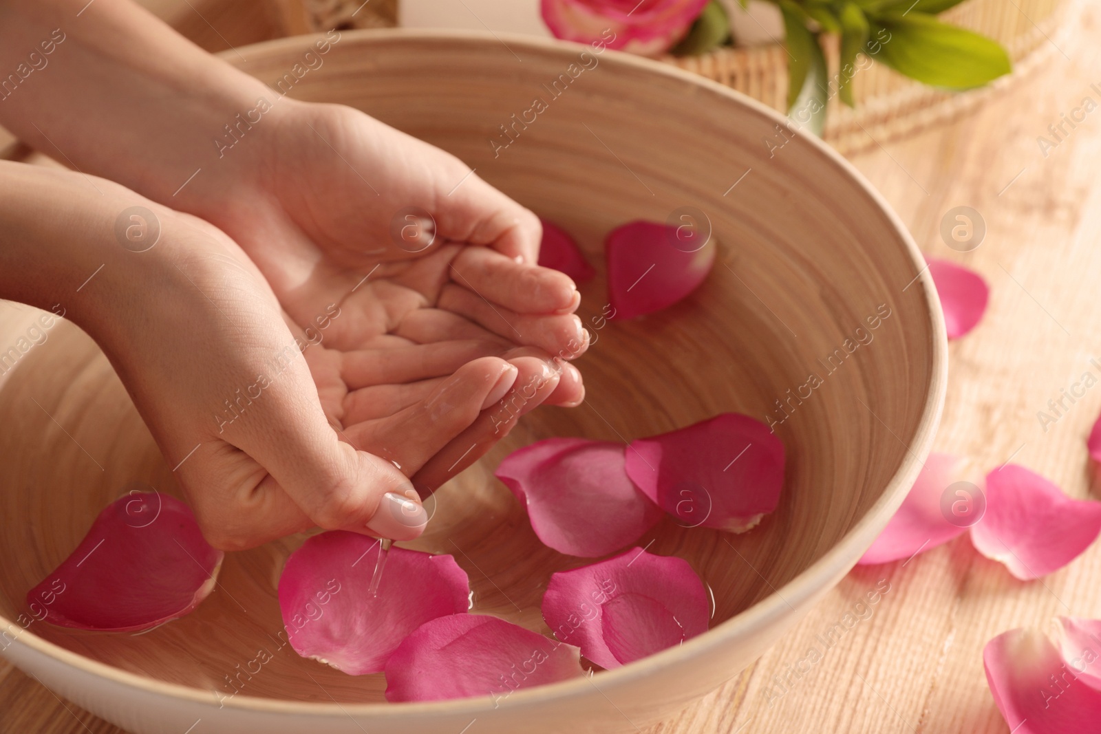 Photo of Woman soaking her hands in bowl of water and petals on table, closeup with space for text. Spa treatment