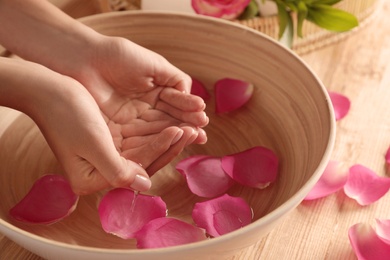 Woman soaking her hands in bowl of water and petals on table, closeup with space for text. Spa treatment