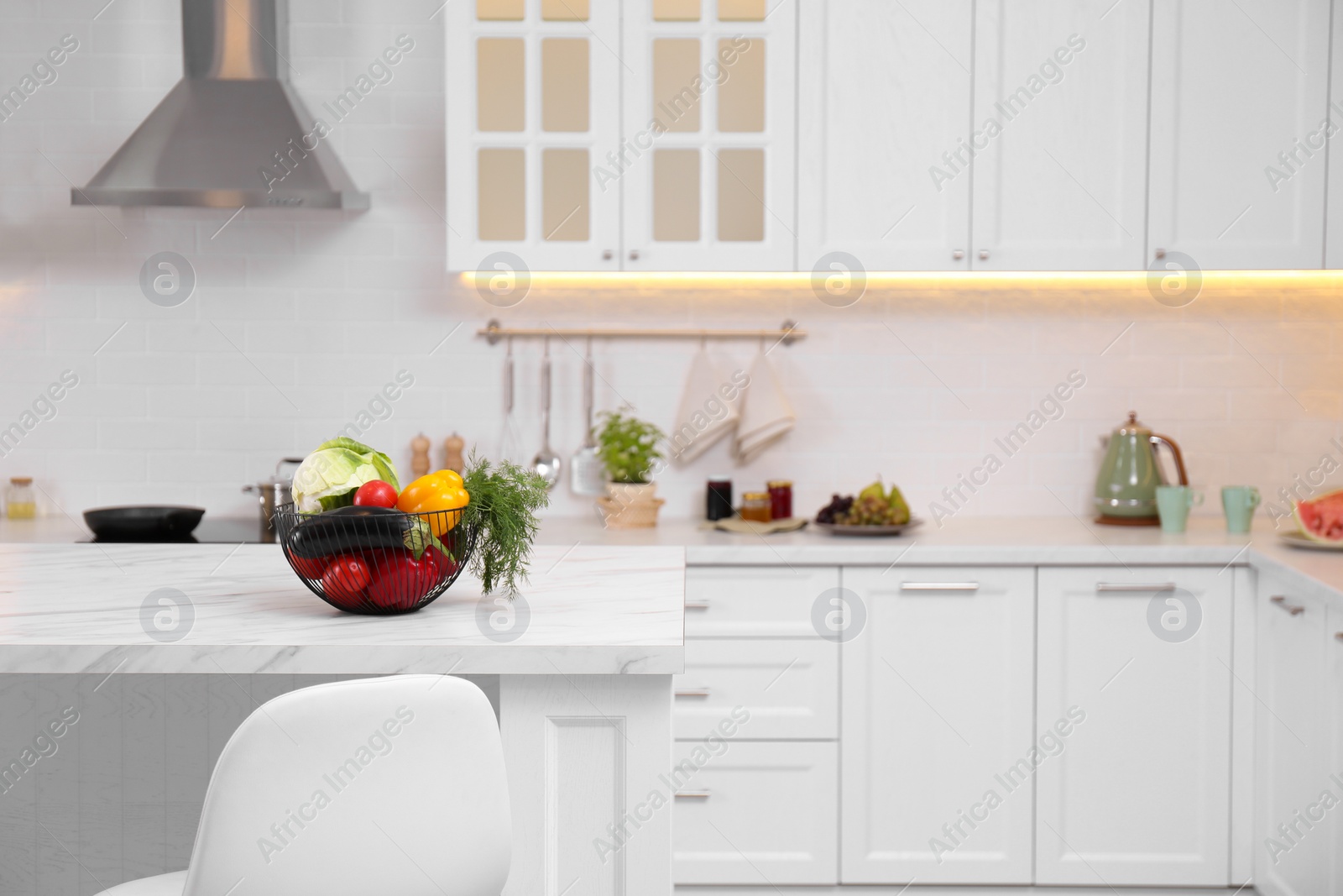 Photo of Basket full of different vegetables on white table in modern kitchen