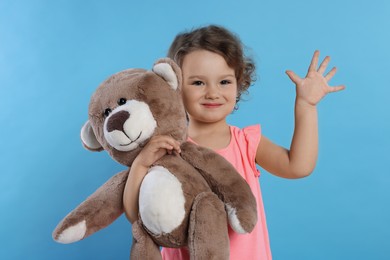 Photo of Cute little girl with teddy bear on light blue background