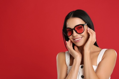 Photo of Beautiful woman wearing sunglasses on red background. Space for text