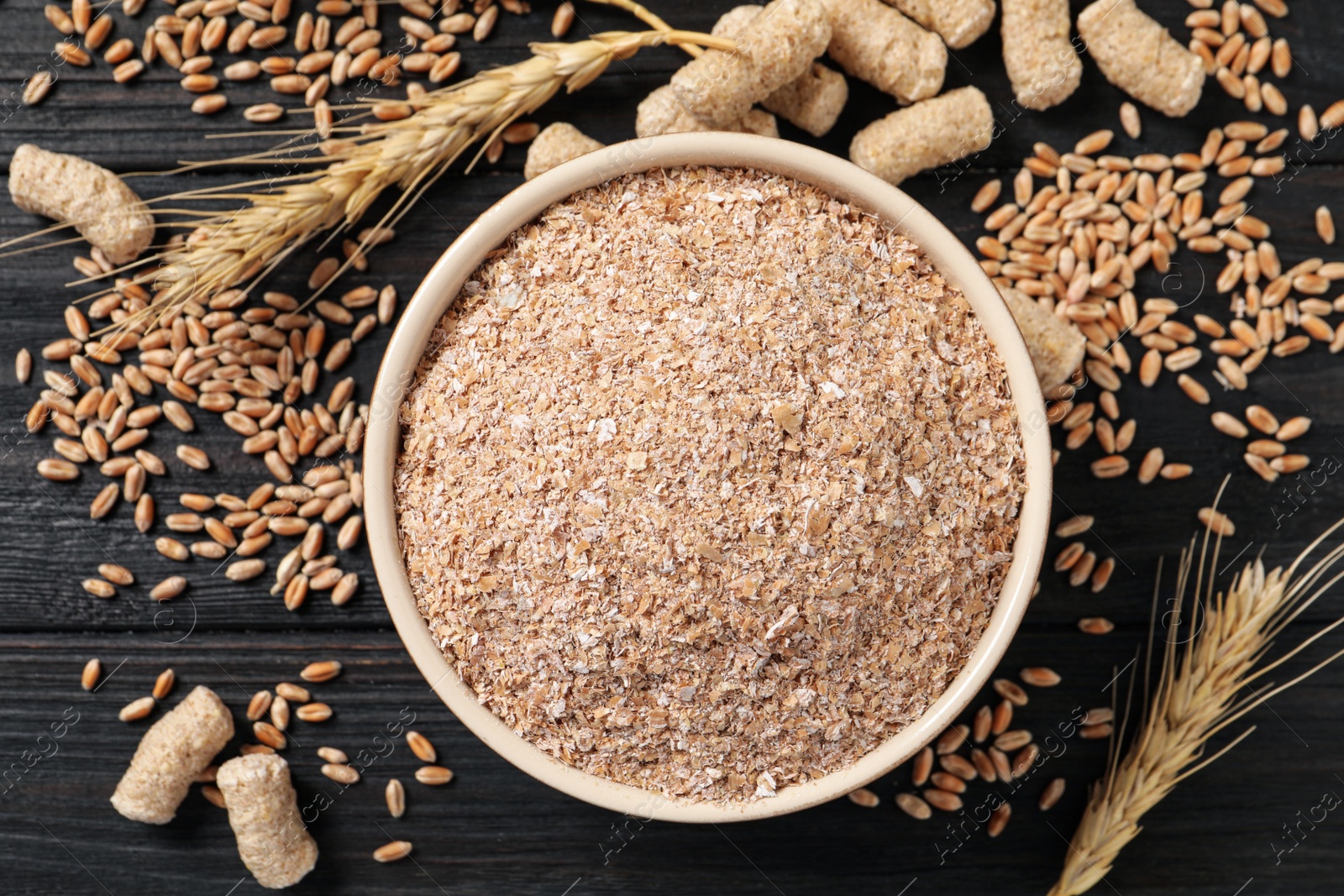 Photo of Bowl of wheat bran on black wooden table, flat lay