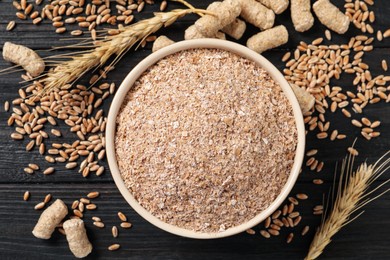 Photo of Bowl of wheat bran on black wooden table, flat lay