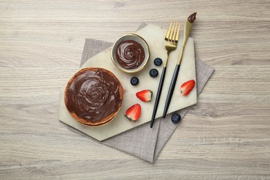 Photo of Delicious pancakes with chocolate paste, berries and cutlery on wooden table, top view