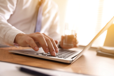 Image of Man working with laptop at table in office, closeup