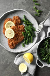 Photo of Tasty schnitzels served with lemon and green beans on grey table, flat lay