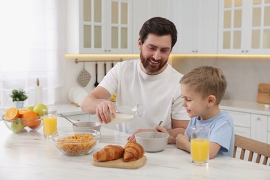 Father and his cute little son having breakfast at table in kitchen