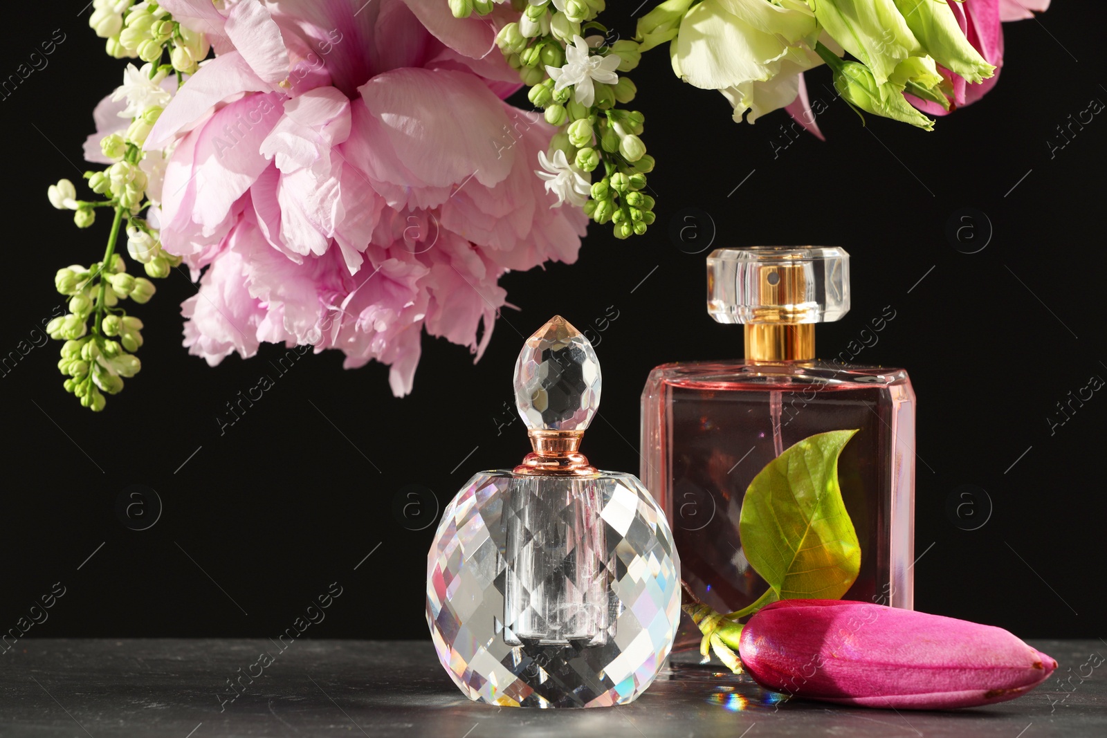 Photo of Luxury perfumes and floral decor on grey table against black background