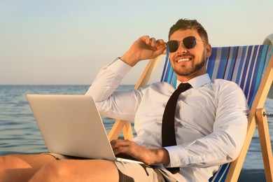 Happy man with laptop on deckchair near sea. Business trip