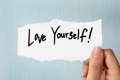 Photo of Woman holding note with words LOVE YOURSELF on light background, closeup