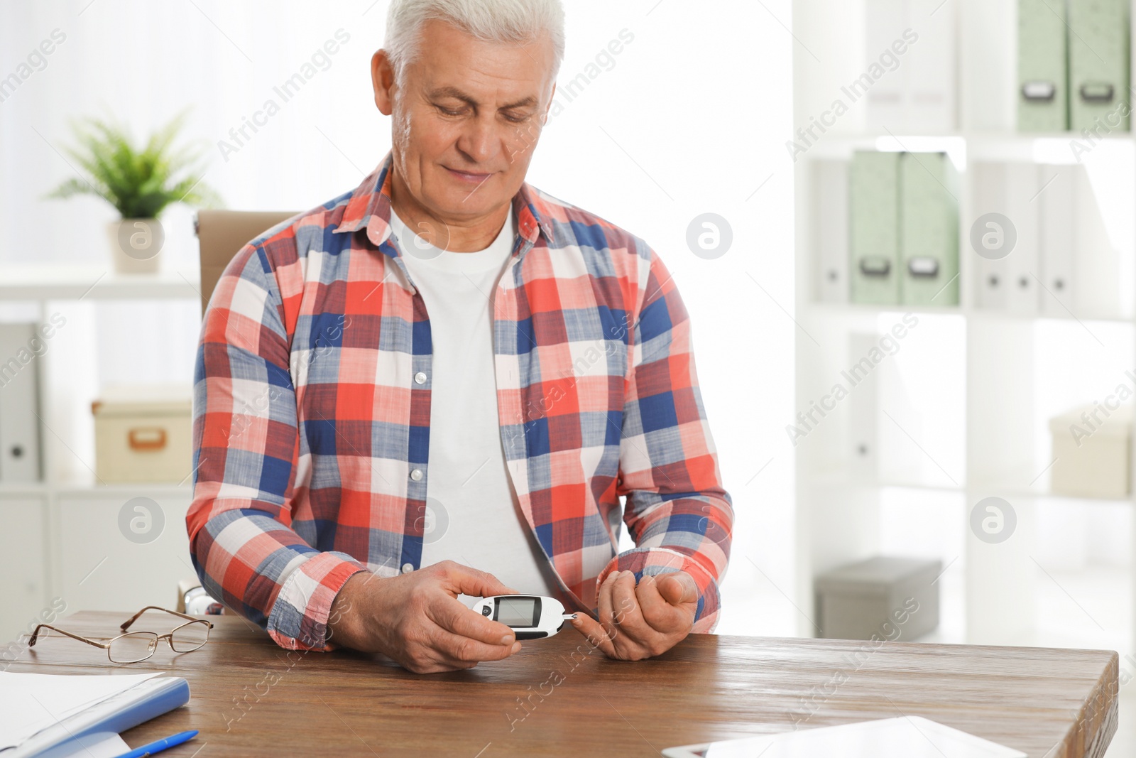 Photo of Senior man using digital glucometer at table. Diabetes control