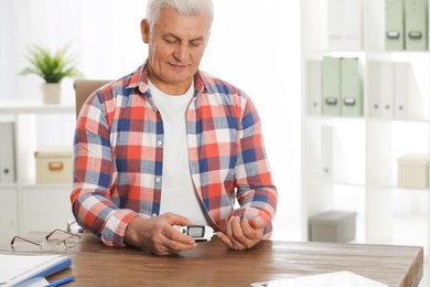Photo of Senior man using digital glucometer at table. Diabetes control